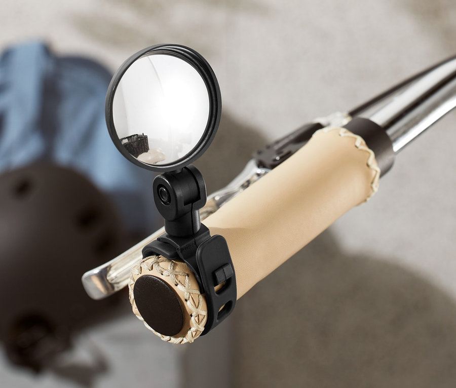 Gros plan d'un guidon de vélo avec un mini-rétroviseur de vélo fixé. Un casque et une veste sont visibles en arrière-plan.