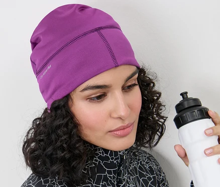 Femme portant un bonnet technique thermique rose baie et tenant une bouteille d'eau blanche.