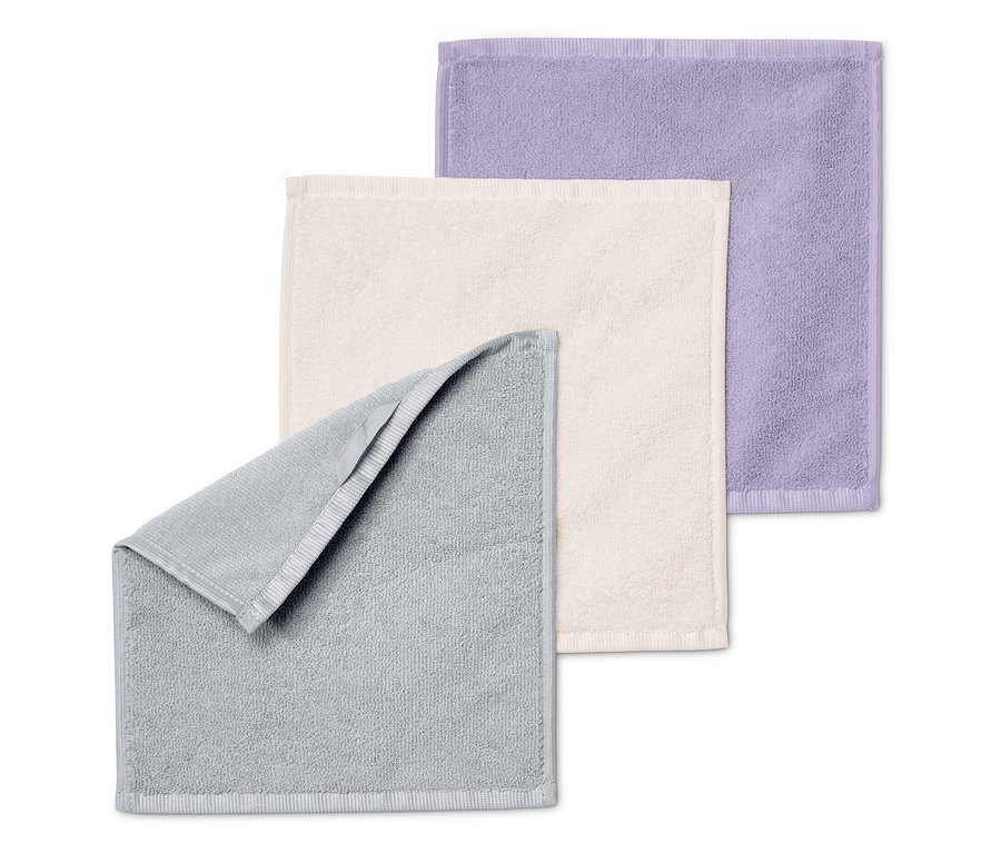 Trois serviettes pliées les unes sur les autres : grise, crème et violette.