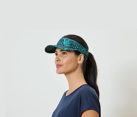 Une femme avec une queue de cheval et un t-shirt bleu porte une visière verte à motifs de feuilles.