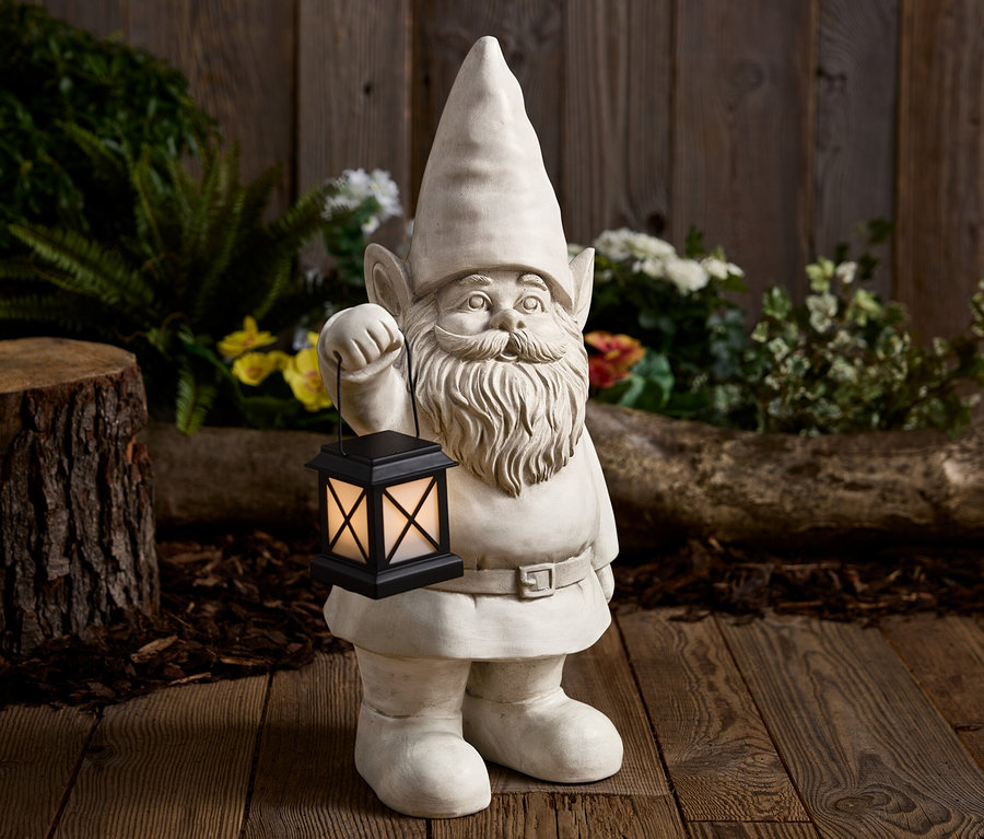 Un nain de jardin en pierre tient une lanterne noire devant un fond en bois.