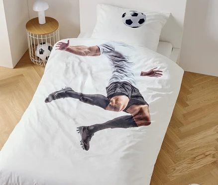 Sur une housse de couette, un joueur de football est représenté en train de sauter, à côté d'une table de chevet avec une lampe et un ballon de football.
