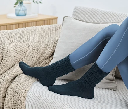 Jambes en leggings bleus et 1 paire de chaussettes-jambières sur un canapé beige.