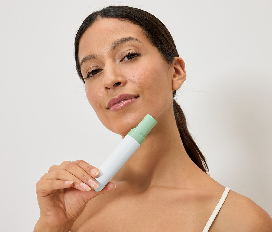 Une femme tient une bouteille blanche et verte devant son visage.