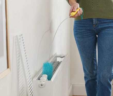 Femme nettoyant un radiateur avec une brosse pour radiateurs.