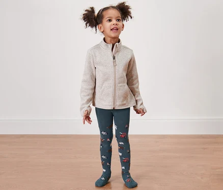 Une petite fille porte 2 collants pour tout petits, ferme/verts.