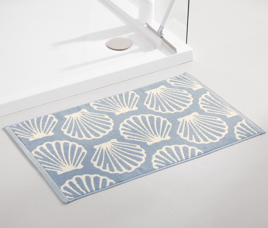 Un tapis de douche bleu clair avec un motif de coquillages est posé à côté d'une douche.