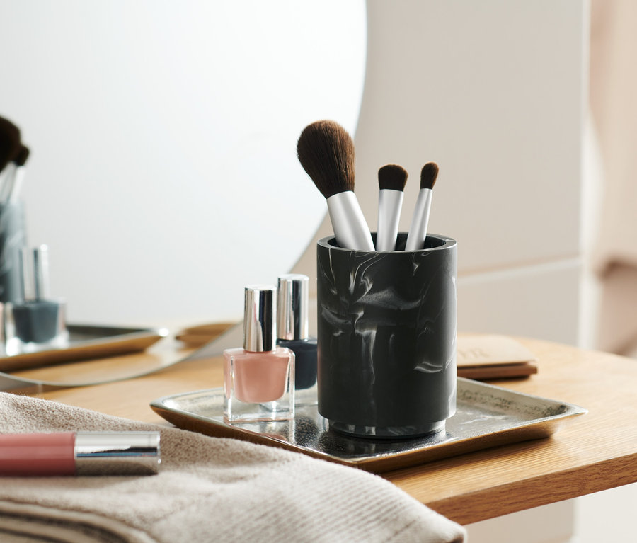 Pinceaux de maquillage dans un pot finition marbrée à côté de vernis à ongles sur un plateau.