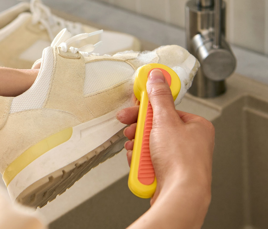 Une femme nettoie une chaussure avec une brosse à chaussures au-dessus d'un lavabo.