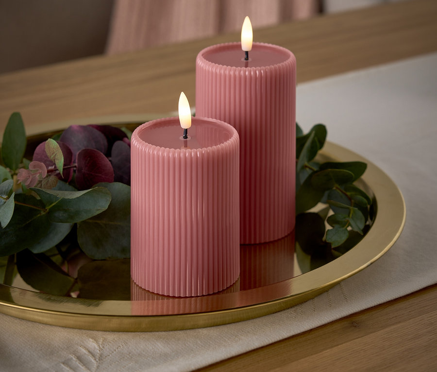 Deux bougies roses avec des flammes sur un plateau doré avec des branches décoratives sur une table.