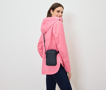 Une femme regarde par-dessus son épaule, portant une veste rose et un sac bandoulière noir.