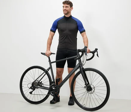 Un homme se tient à côté d'un vélo et porte un maillot de cyclisme bleu.
