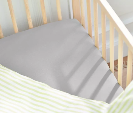 Gros plan d'un lit de bébé avec un drap-housse gris et un oreiller à rayures vertes.