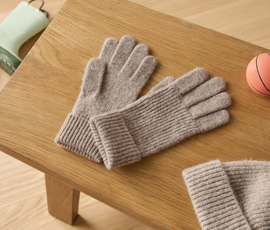 Sur une table en bois reposent une paire de gants tricotés gris, une paire de bottes en caoutchouc vertes et un petit ballon de basket orange.