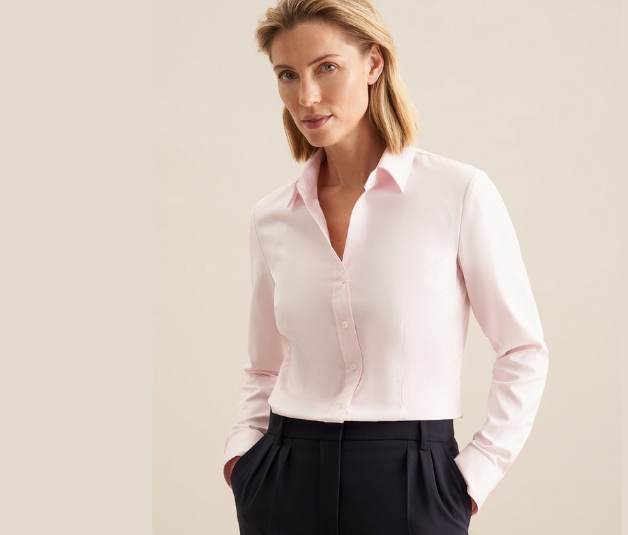 Une femme porte un chemisier en tulle rose Seidensticker et un pantalon bleu marine.