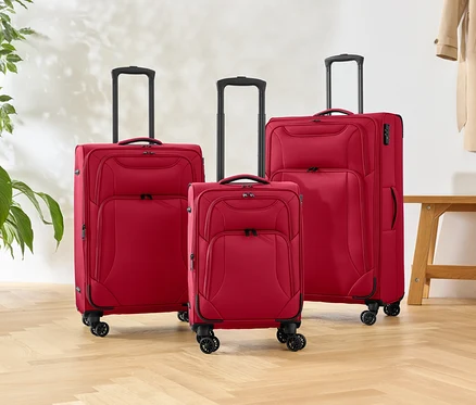 Trois valises rouges à roulettes de différentes tailles sont posées sur un parquet, à côté d'une plante et d'un banc.