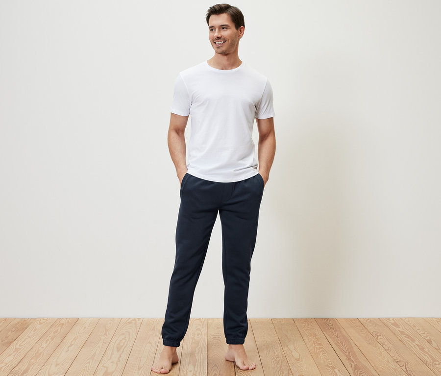 Un homme debout, les mains dans les poches de son pantalon en sweat.