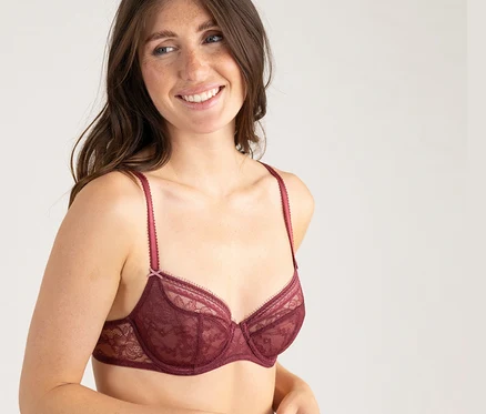 Femme souriante aux cheveux longs portant un soutien-gorge demi-bonnet en dentelle bordeaux Passionata « Jeanne ».