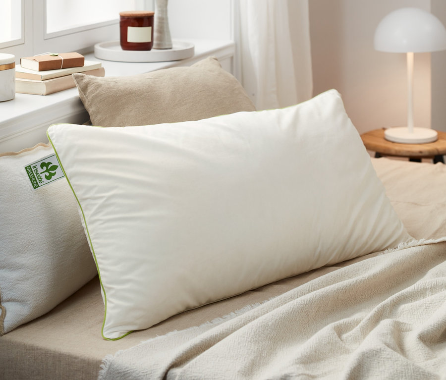 Plusieurs oreillers en plumes irisette® greenline de différentes tailles sont posés sur un lit.