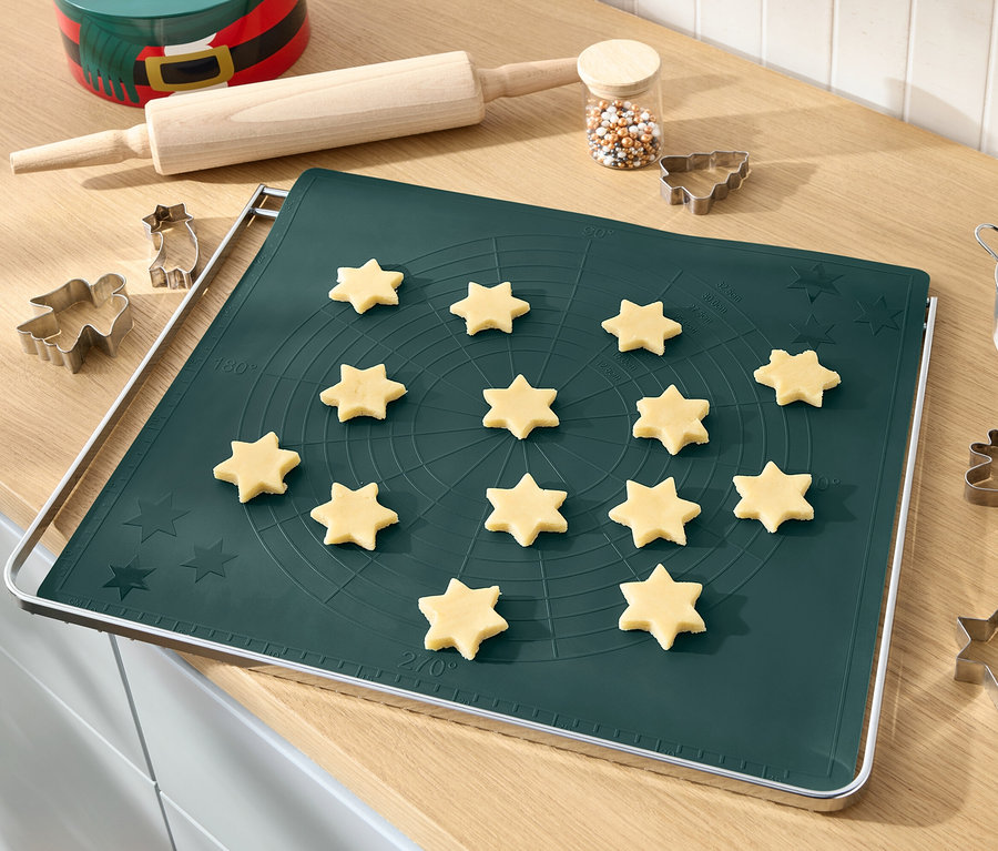 Étoiles de pâte sur un tapis de cuisson vert avec rouleau à pâtisserie, vermicelles décoratifs et emporte-pièces.