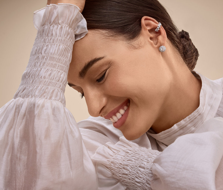 Femme souriante avec des boucles d'oreilles et un piercing à l'oreille, la tête appuyée sur sa main.
