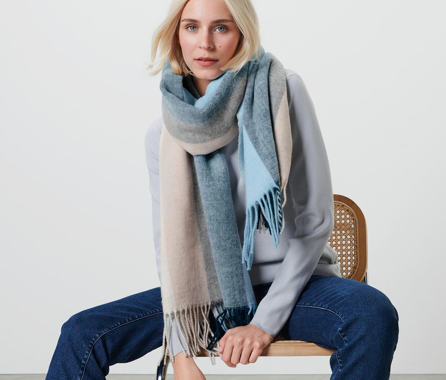 Une femme blonde est assise sur une chaise et porte une écharpe tissée à rayures.