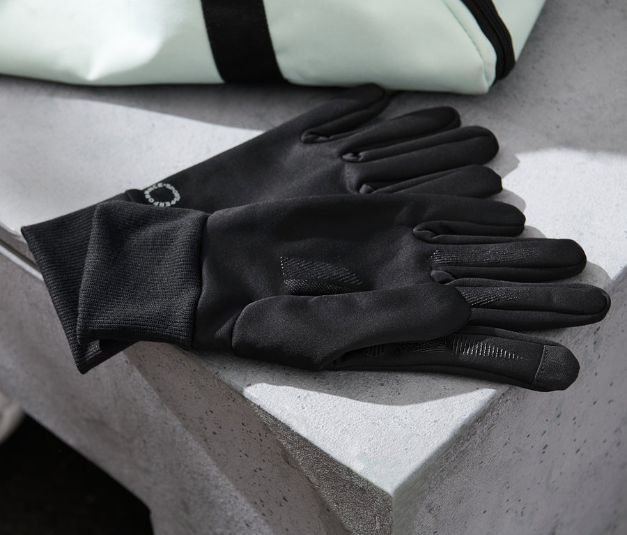 Des gants coupe-vent noirs sont posés sur une surface en béton à côté d'un ballon blanc et d'un sac.