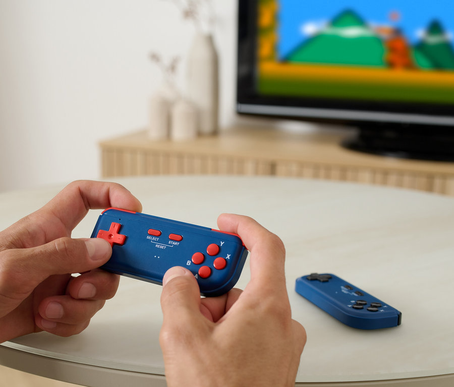 Un homme joue à la console rétro pour télé, un téléviseur est visible en arrière-plan.