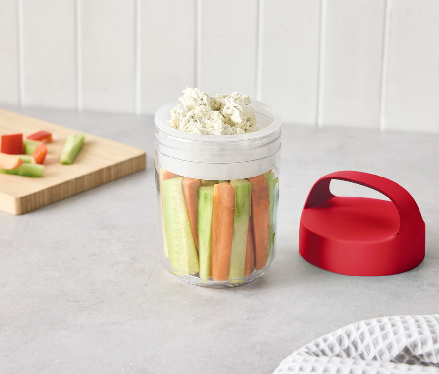 Un verre avec des légumes coupés et une sauce sur une table.