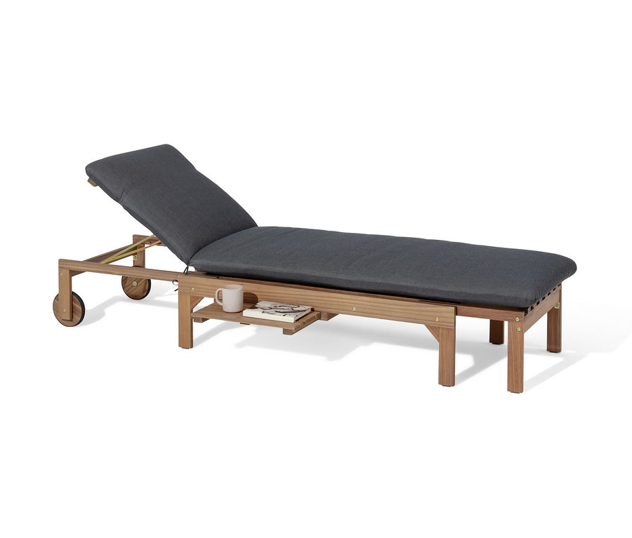 Une chaise longue extensible « Tinus » avec matelas de qualité supérieure, des roues et une petite table, sur laquelle il y a une tasse et un livre.