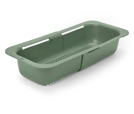 Un égouttoir extensible en plastique vert olive est posé en diagonale sur une surface blanche.