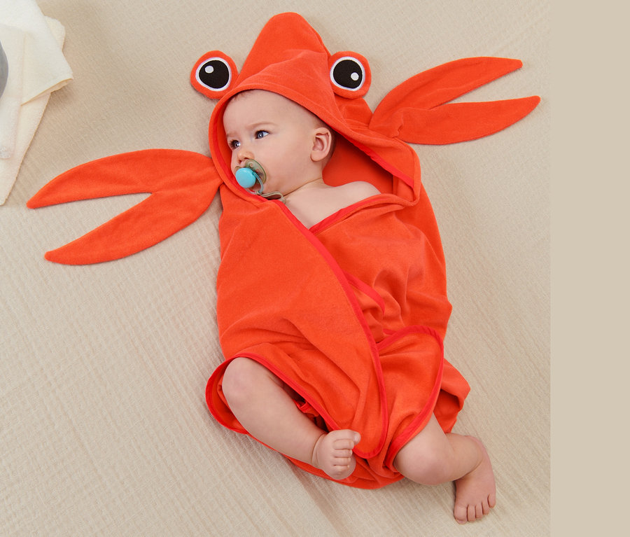 Bébé allongé sur une couverture, enveloppé dans une serviette à capuche en forme de crabe orange.