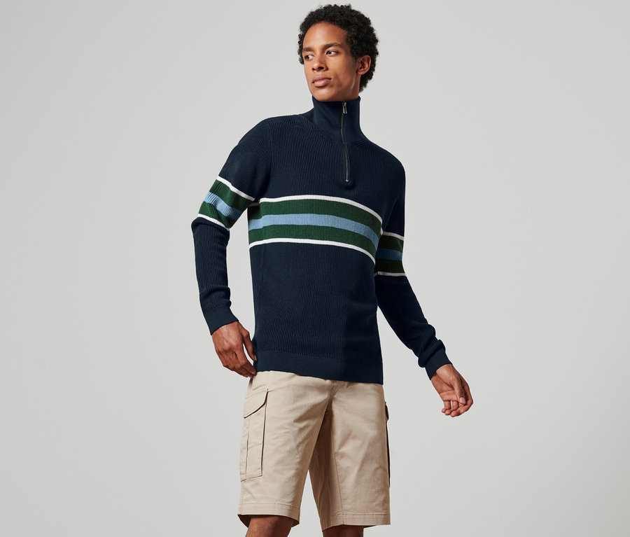 Un homme porte un pull camionneur bleu marine à rayures avec un short kaki.