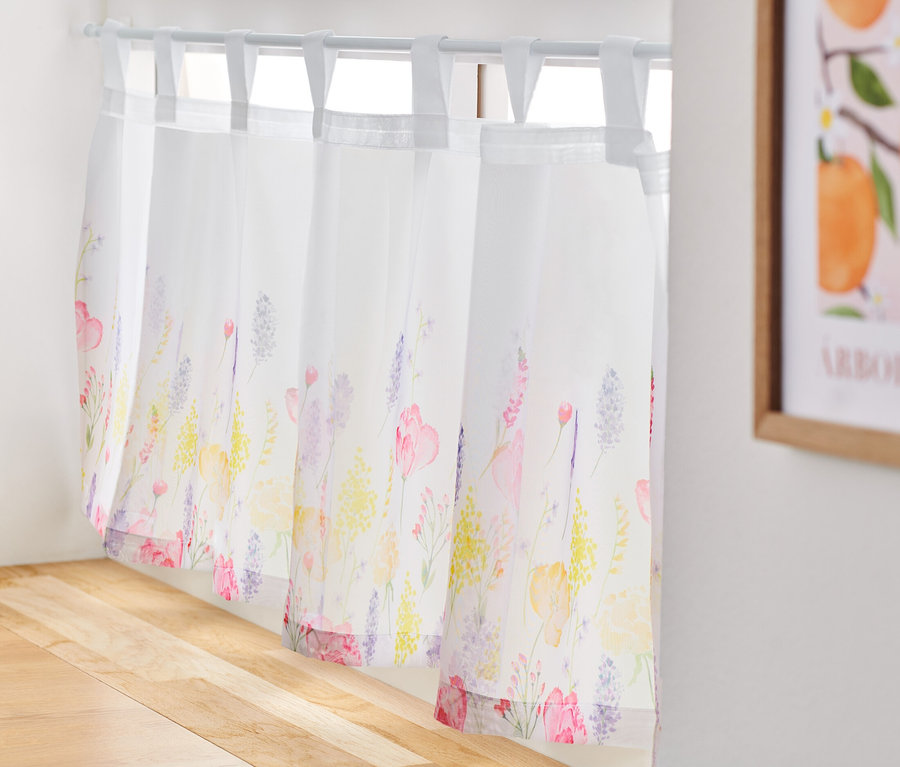 Un rideau de bistrot imprimé est suspendu à une fenêtre.