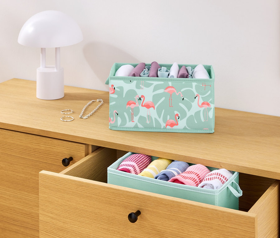 Sur une commode, il y a 2 boîtes de rangement pour tiroir, une avec des flamants roses et une avec des vêtements.