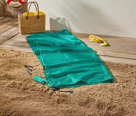 Une serviette de plage verte est posée sur le sable, à côté d'un masque de plongée jaune et d'un panier en osier.