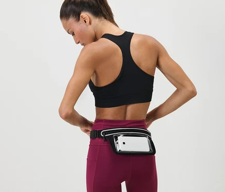 Femme ajustant une Ceinture de course pour smartphone autour de sa taille. Elle porte un soutien-gorge de sport et des leggings.
