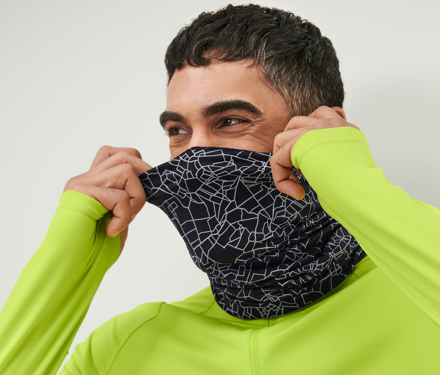 Un homme enfile un foulard multifonction noir réfléchissant sur son visage.