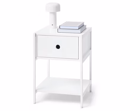 Table de chevet blanche avec un tiroir, une lampe et deux livres dessus.
