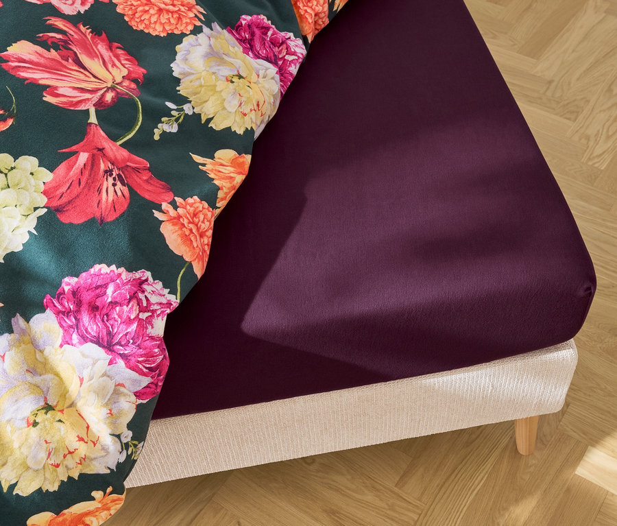 Lit avec drap-housse violet et linge de lit à fleurs.