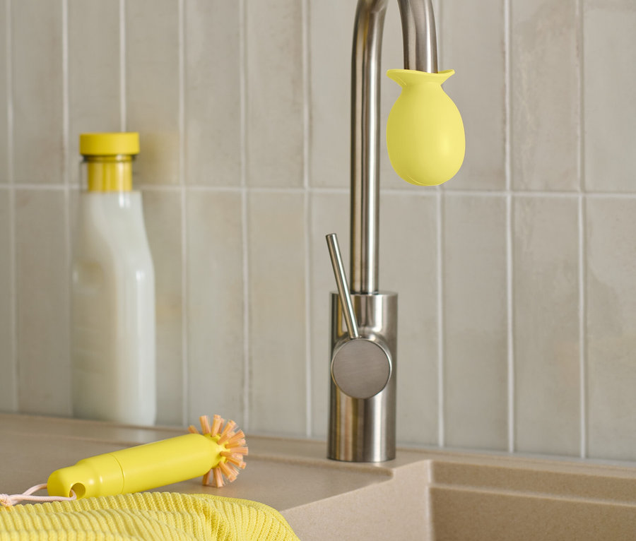 Un robinet en acier inoxydable avec une éponge jaune, une brosse jaune et un chiffon sont posés sur l'évier à côté d'une bouteille.