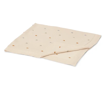 Une couverture pour bébé crème avec des points brodés colorés est pliée sur une surface blanche.