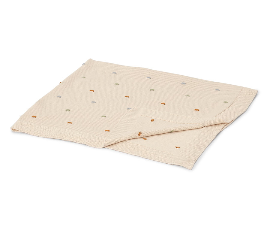 Une couverture pour bébé crème avec des points brodés colorés est pliée sur une surface blanche.
