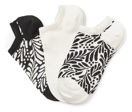 Trois chaussettes sont côte à côte : une noire avec un motif de feuilles blanches, une blanche et une blanche avec un motif de feuilles noires.