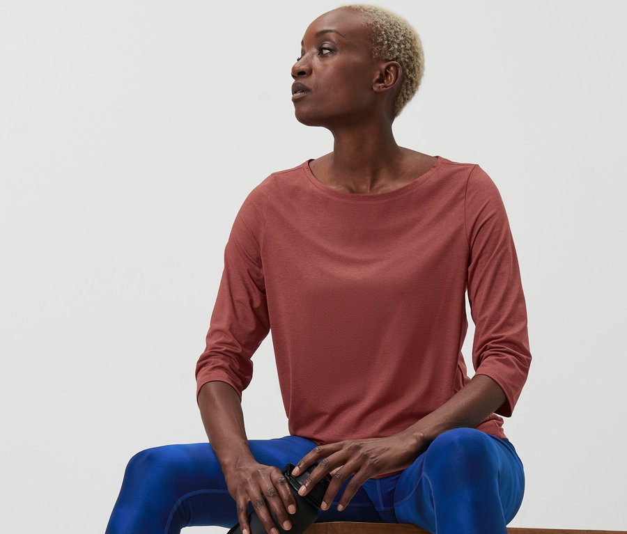 Femme assise sur un banc tenant une bouteille d'eau. Elle porte un t-shirt fonctionnel terre cuite à manches 3/4.