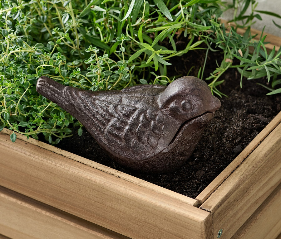 Une cachette pour clés marron en forme d'oiseau dans un pot de fleurs en bois avec des plantes.