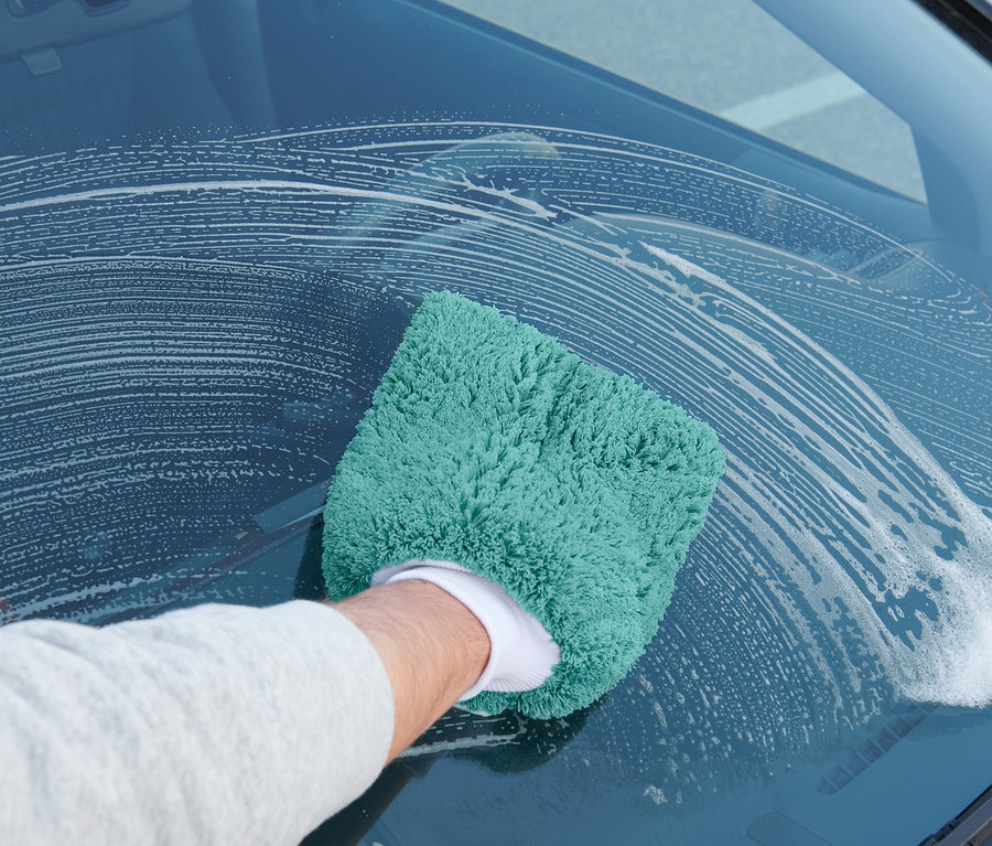 Un homme nettoie le pare-brise d'une voiture avec un gant de lavage voiture.
