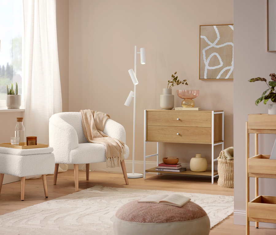 Un fauteuil bouclette avec pieds en bois est placé à côté d'un lampadaire Trio »Soka«. Un tapis gris »Cosmo «Waves est posé sur le sol.