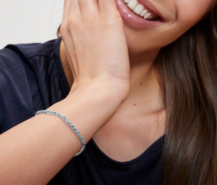 Une femme souriante touche son visage et porte un bracelet de tennis avec chaîne Paperlink.