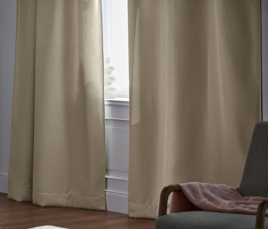 Chambre avec 2 rideaux occultants beiges à la fenêtre, un lit et un fauteuil gris.